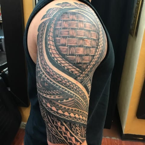 Black Polynesian bands and woven patterns wrap around a shoulder and upper arm.