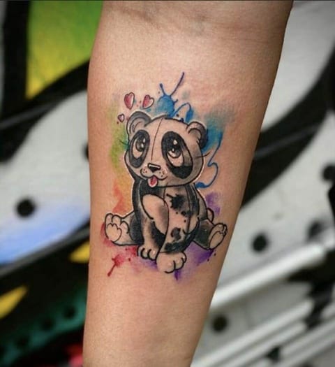 A cartoon panda with hearts and rainbow watercolor splashes sits on a forearm.