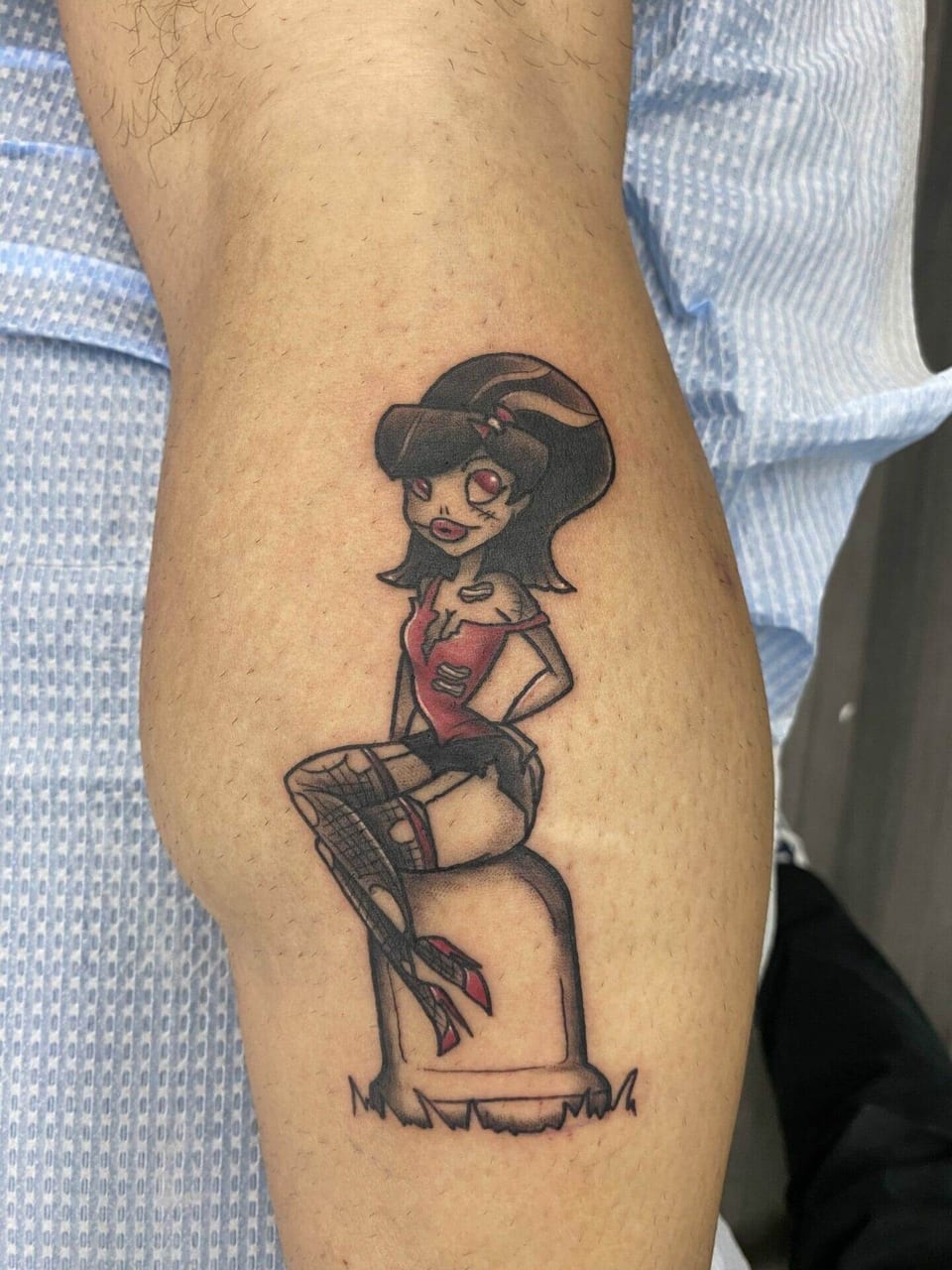 A cartoon zombie pin-up in a red top sits on a gravestone on a calf.
