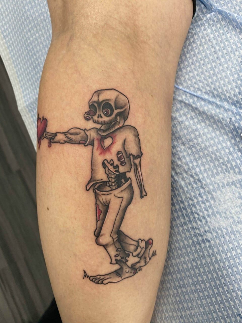 An illustrative skeleton in torn clothes holds a red heart on a calf.