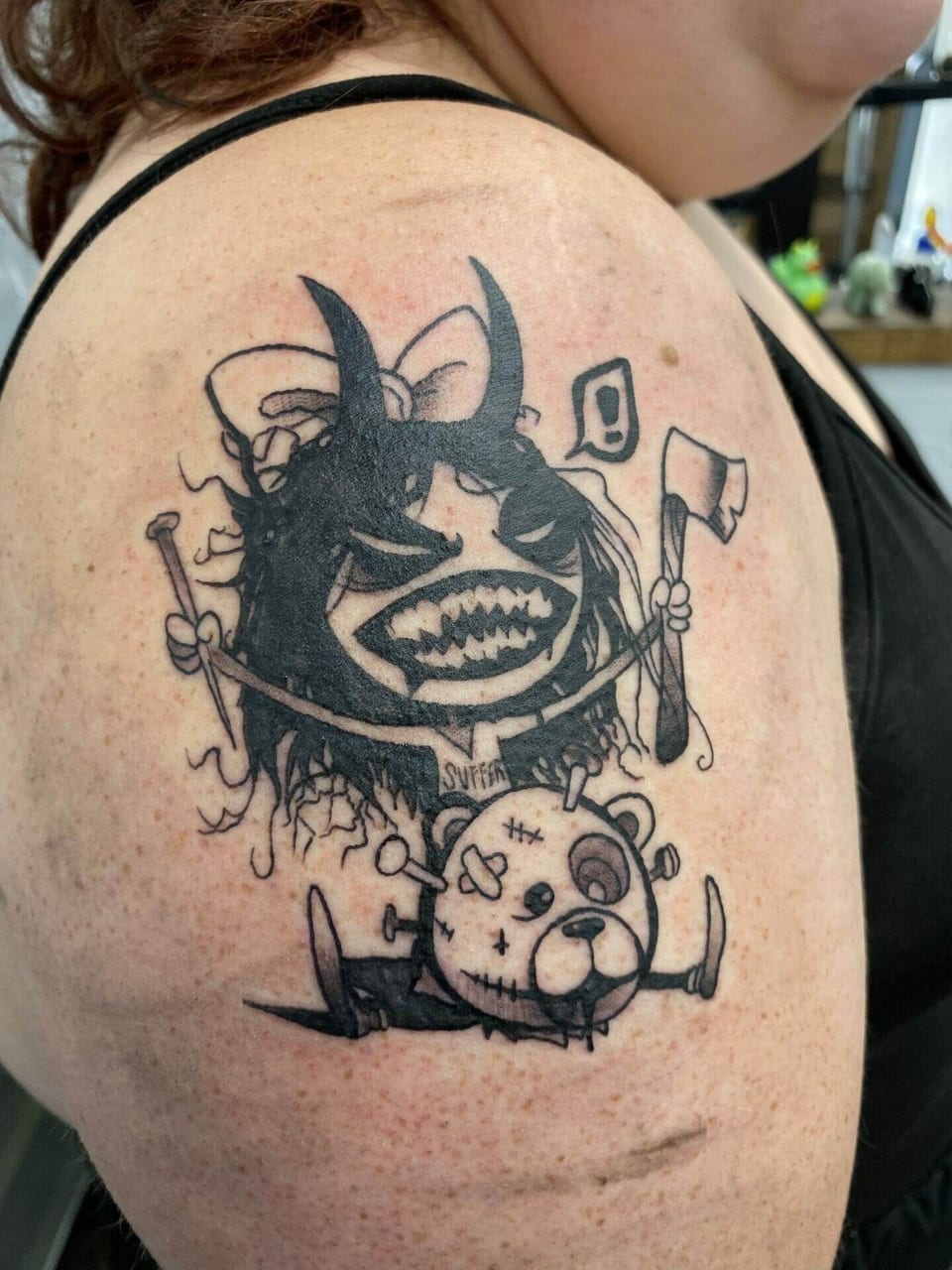 A blackwork horned cartoon figure and stitched teddy bear sit on an upper arm.