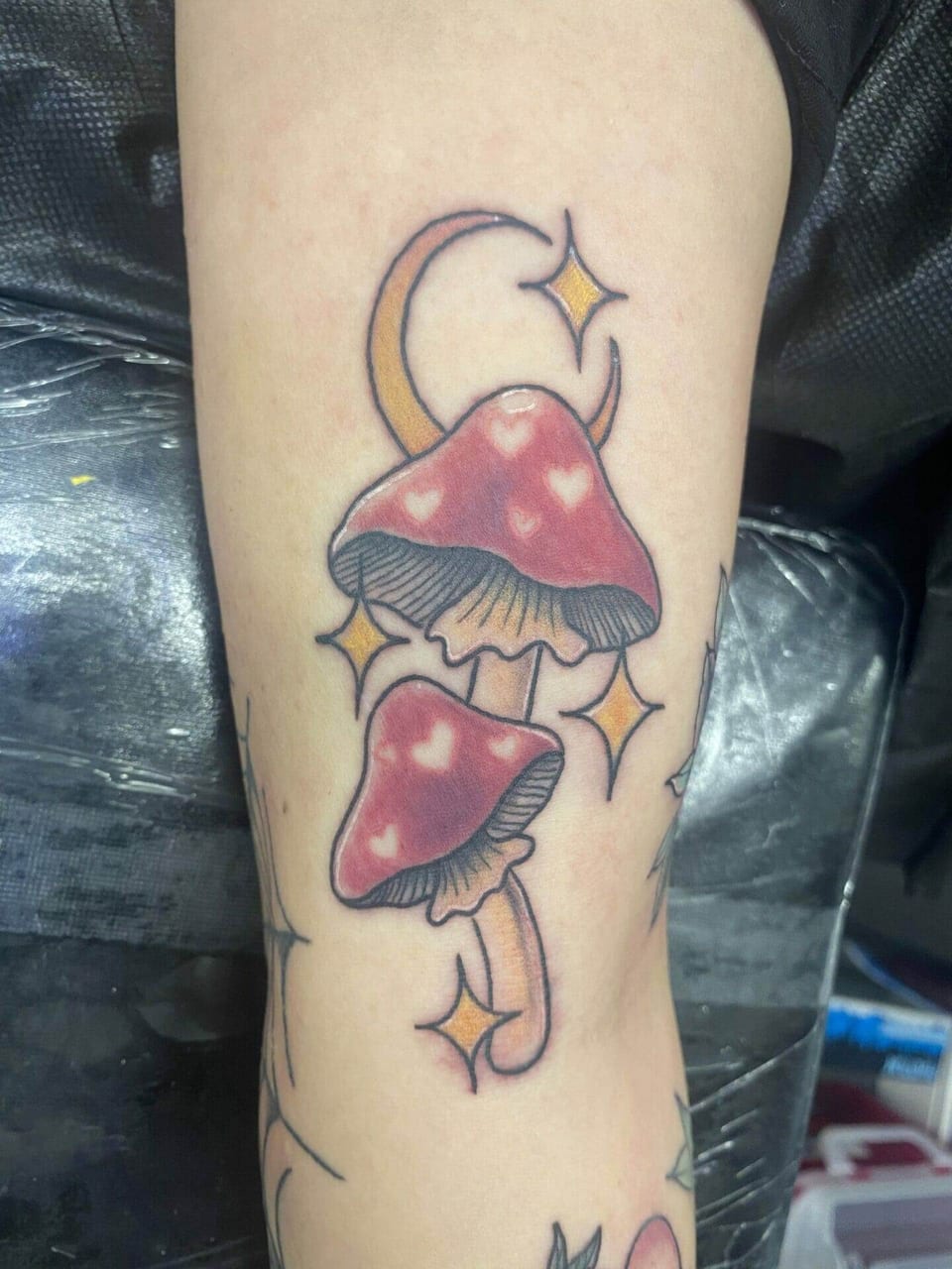 Traditional pink mushrooms with hearts, stars and a crescent moon sit on a forearm.