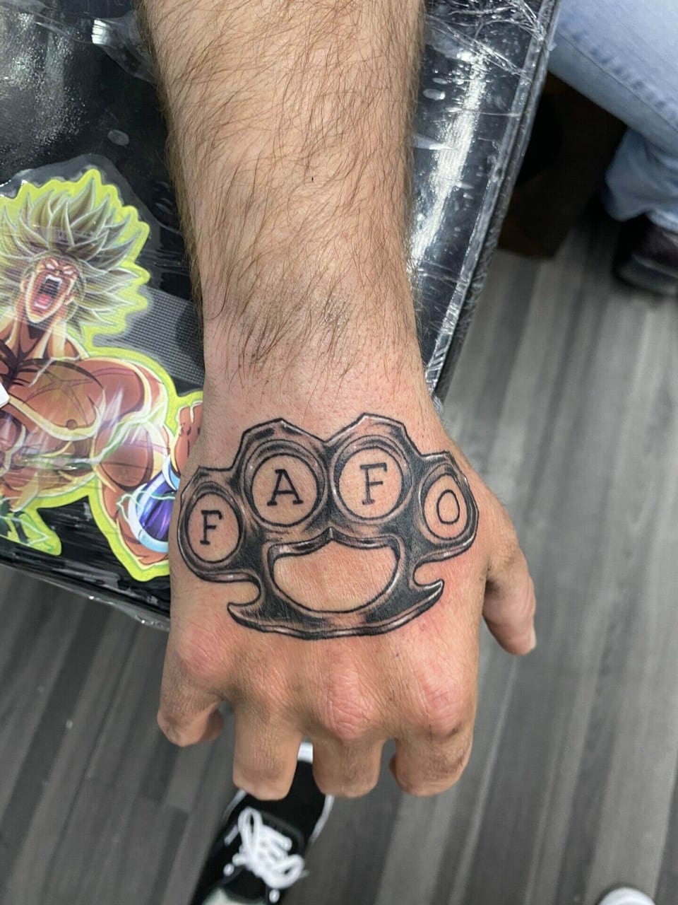 Black and grey brass knuckles reading 'FAFO' cover the back of a hand.