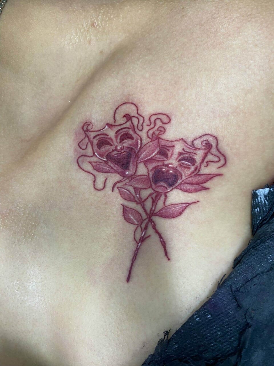 Red linework theater masks with leafy stems sit below a collarbone.