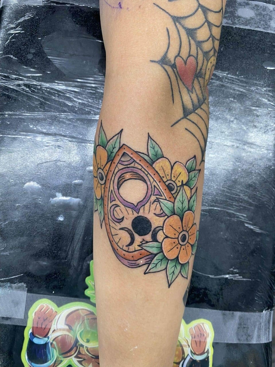 A traditional planchette surrounded by yellow flowers sits on a forearm.