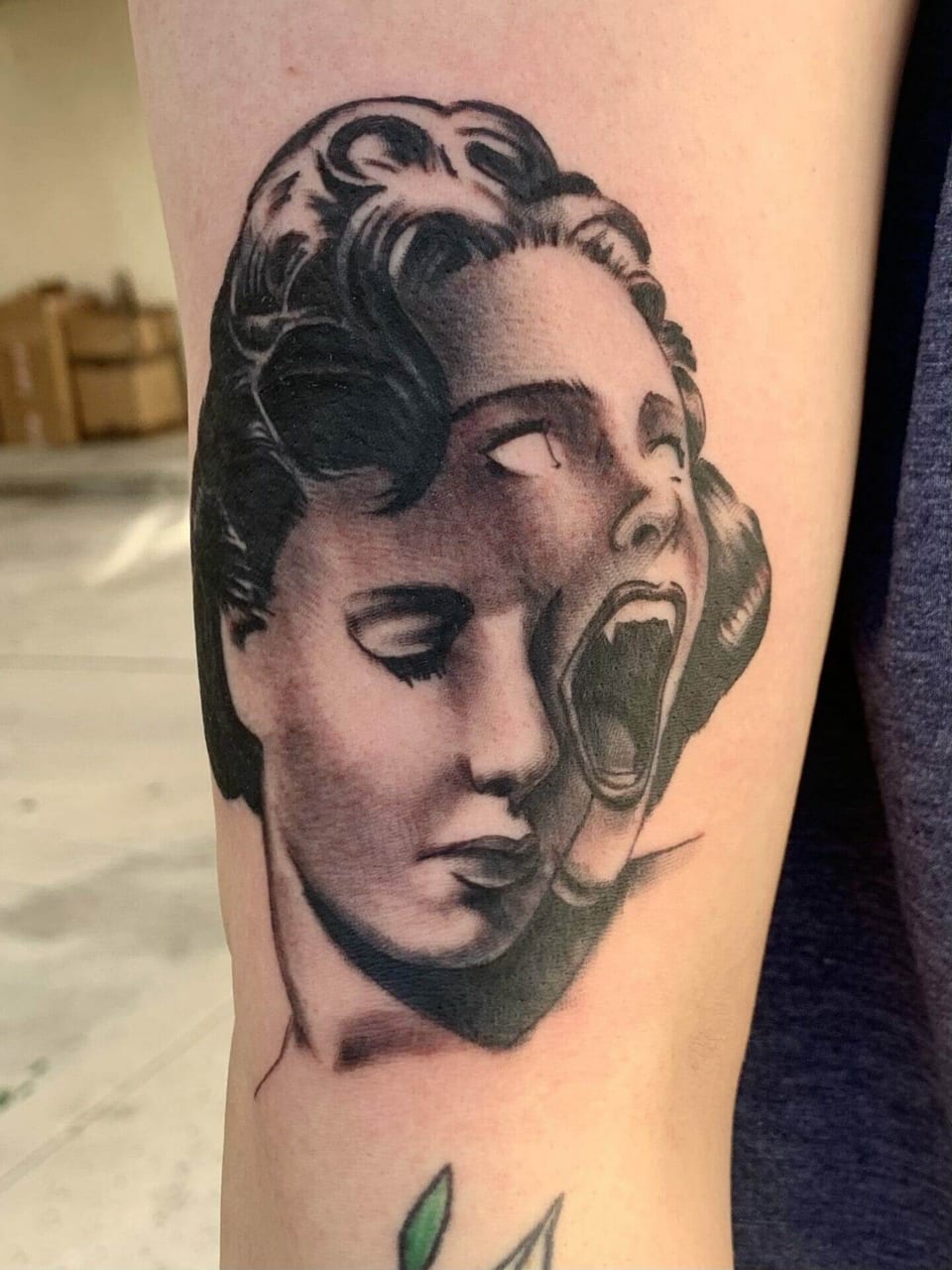 A black and grey woman's face splits into a screaming face on the upper arm.