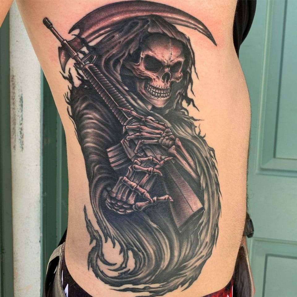 A black and grey grim reaper holds a rifle beneath a scythe on the ribs.