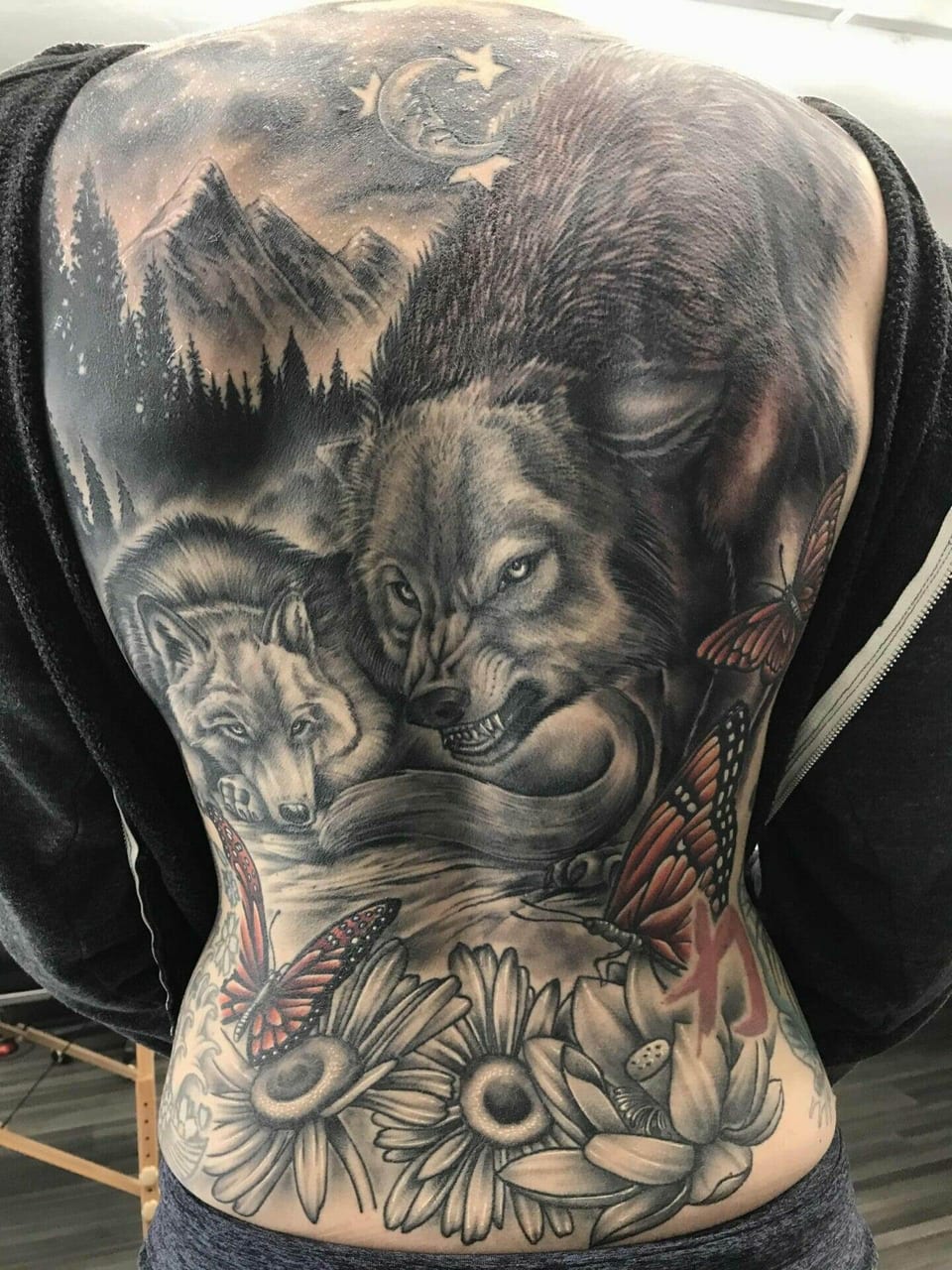 Black and grey wolves, mountains and flowers share a back tattoo with orange butterflies.