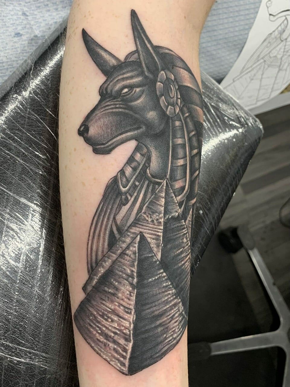 A black and grey Anubis portrait rises above pyramids on the calf.
