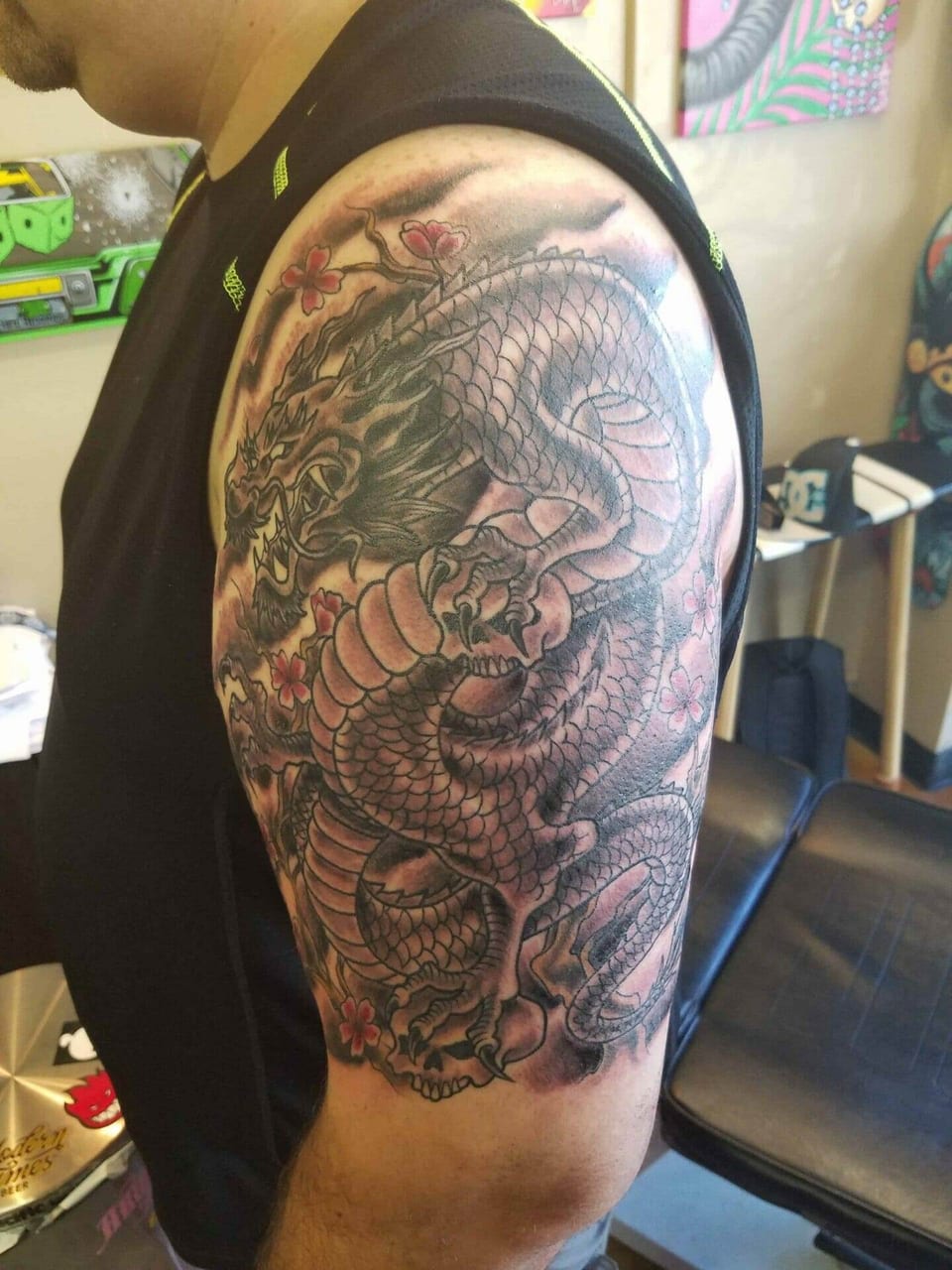 A Japanese black and grey dragon coils among pink blossoms on the upper arm.