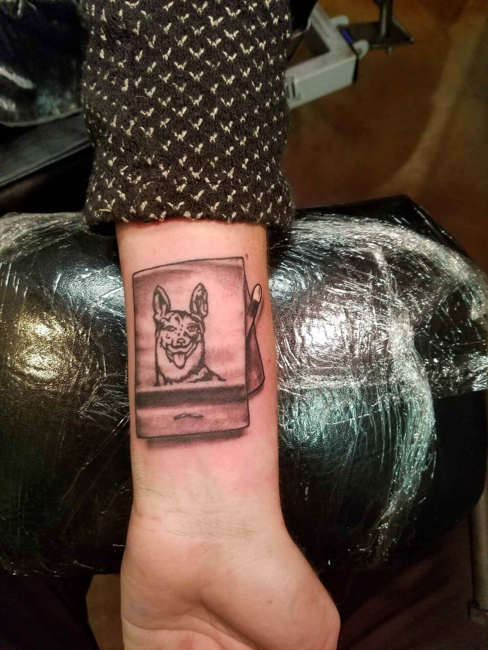 A black and grey dog portrait sits inside an instant-picture frame on the forearm.