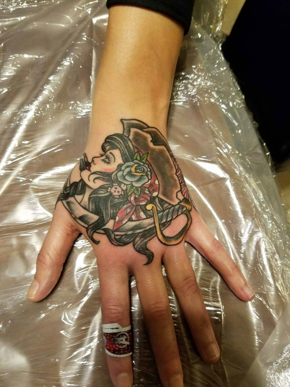 A traditional color pirate woman in a hat with a flower and sword covers the back of the hand.