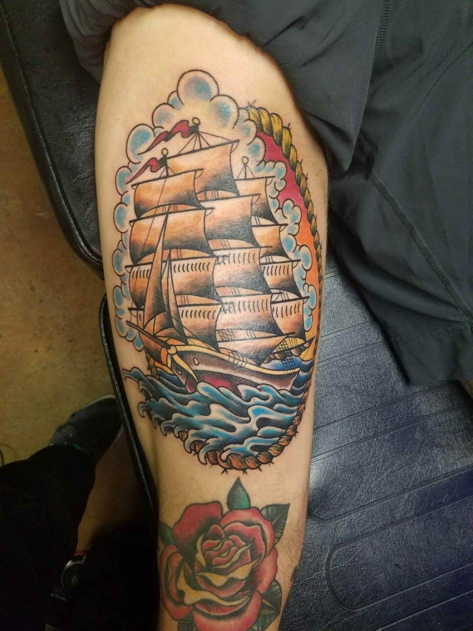 A traditional color sailing ship, waves and rope frame sit above a rose on the thigh.