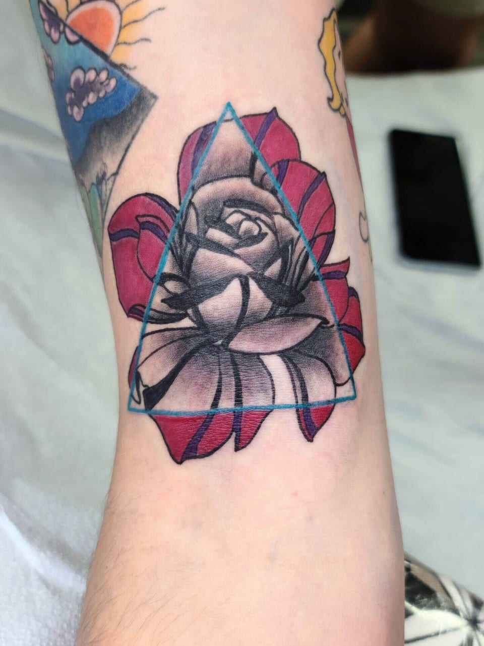 A black and grey rose sits within a blue triangle over red petals on the upper arm.
