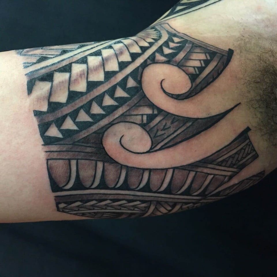 A black Polynesian band combines geometric rows and large uninked spirals on the inner upper arm.
