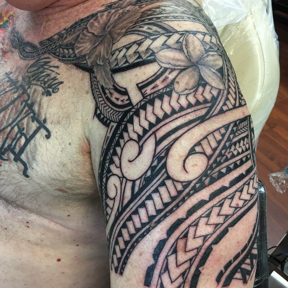 Black Polynesian patterns and plumeria flowers wrap across the chest, shoulder and upper arm.