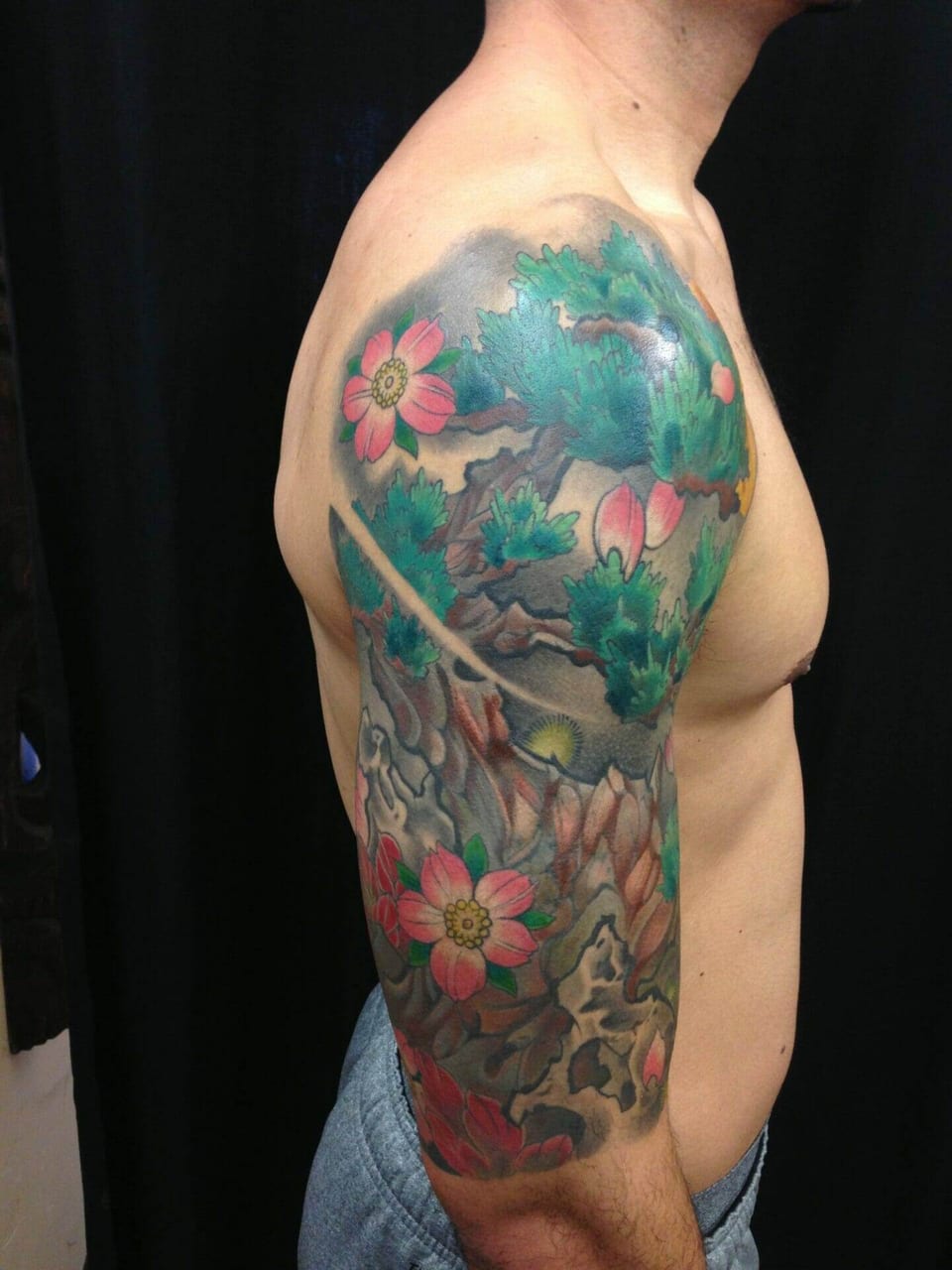 A color Japanese pine tree, pink blossoms and rocks cover the shoulder and upper arm.