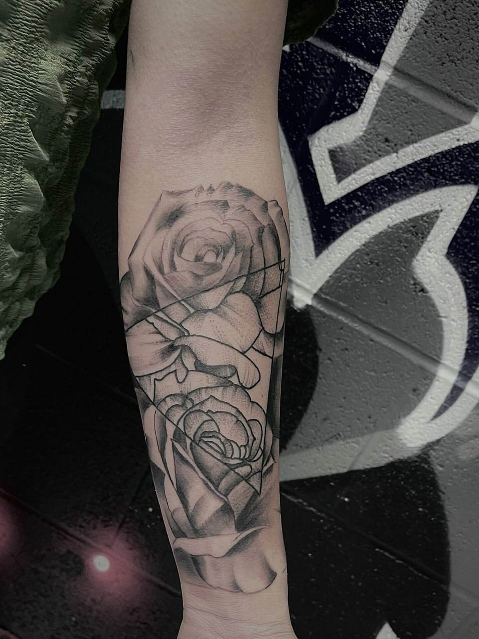 Black and grey roses overlap angular linework in a forearm tattoo.
