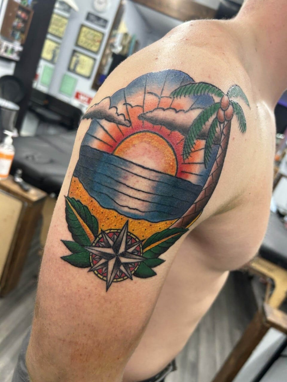 A traditional beach sunset tattoo includes a palm tree and compass rose on a shoulder.