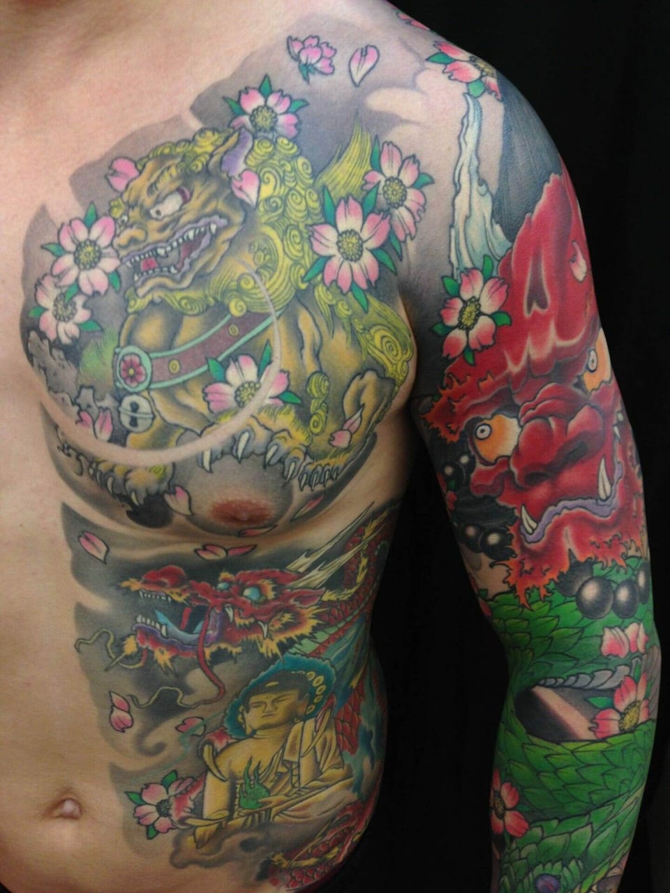 A Japanese tattoo spans the chest, ribs and arm with a guardian lion, dragon, Buddha and cherry blossoms.