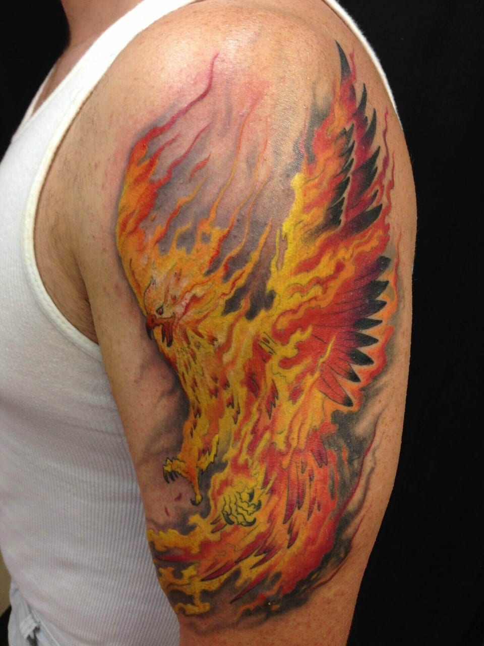 An illustrative phoenix tattoo spreads orange and yellow flaming wings across an upper arm.