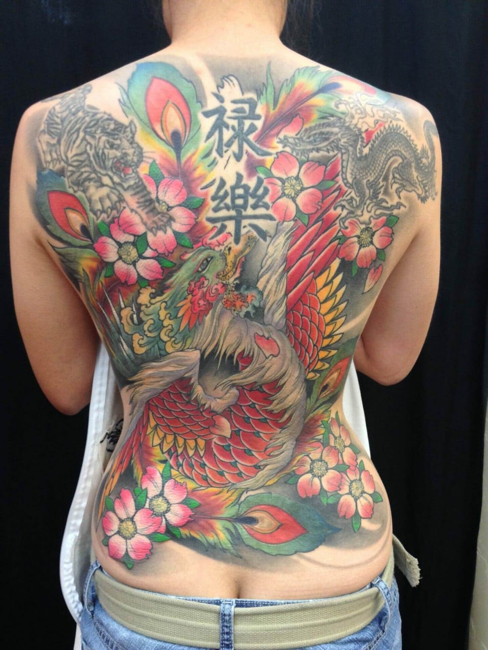 A Japanese full-back tattoo combines a phoenix, tiger, dragon, cherry blossoms and vertical lettering.