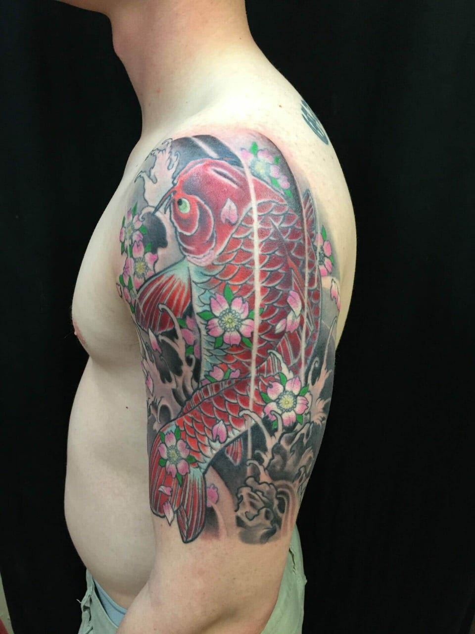 A Japanese red koi tattoo winds through pink cherry blossoms and black waves on an upper arm.