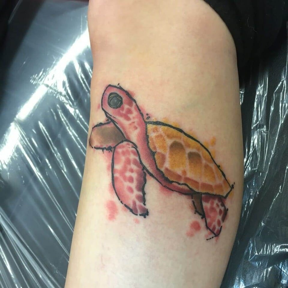 A watercolor sea turtle tattoo combines pink flippers with an orange shell on a lower leg.