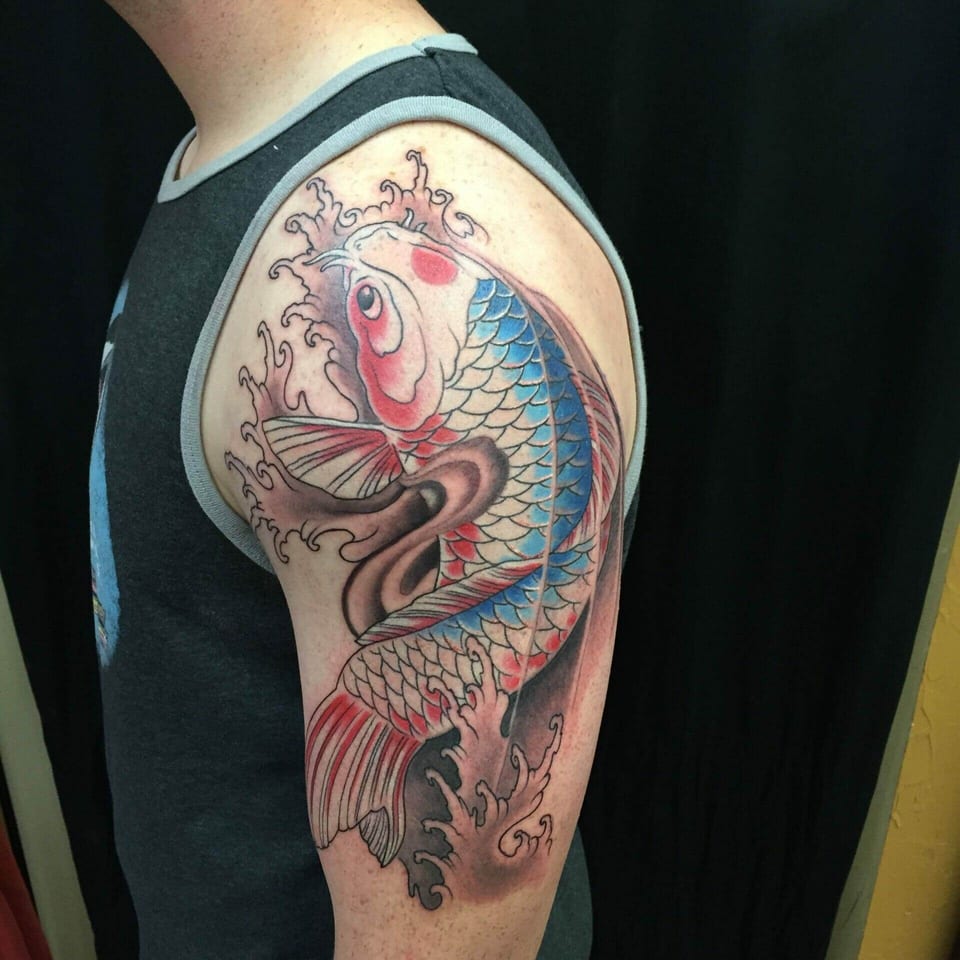 A Japanese blue and white koi tattoo has red markings amid curling waves on an upper arm.