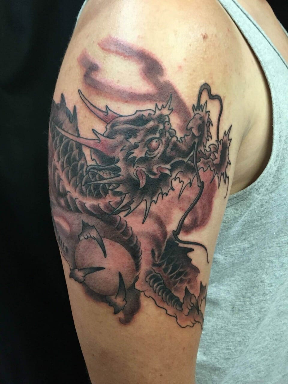 A black and grey Japanese dragon tattoo has red accents and curling whiskers on an upper arm.
