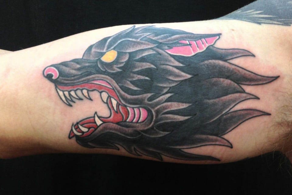 A traditional black wolf head with a red mouth and yellow eye stretches along the inner upper arm.