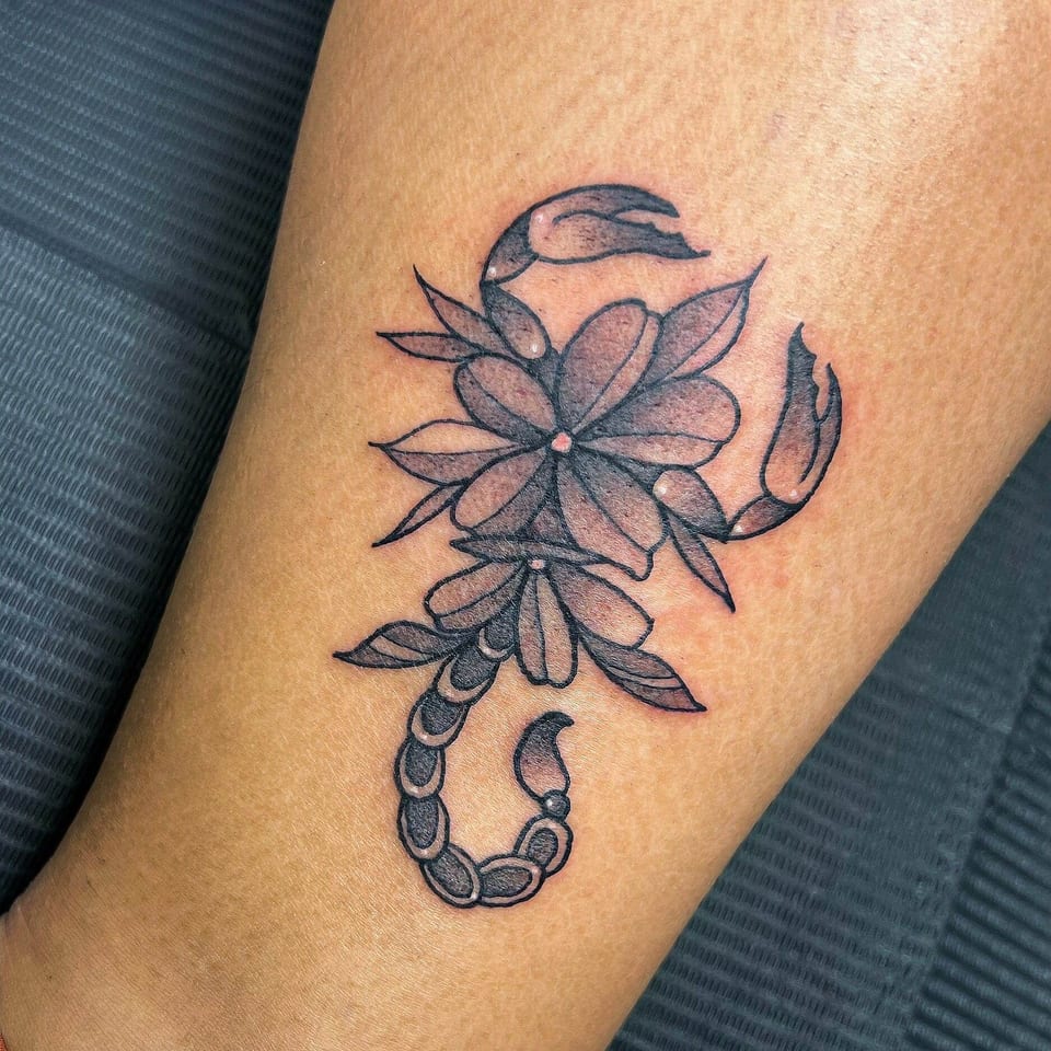 A black and grey scorpion has flowers and leaves forming its body on a forearm.