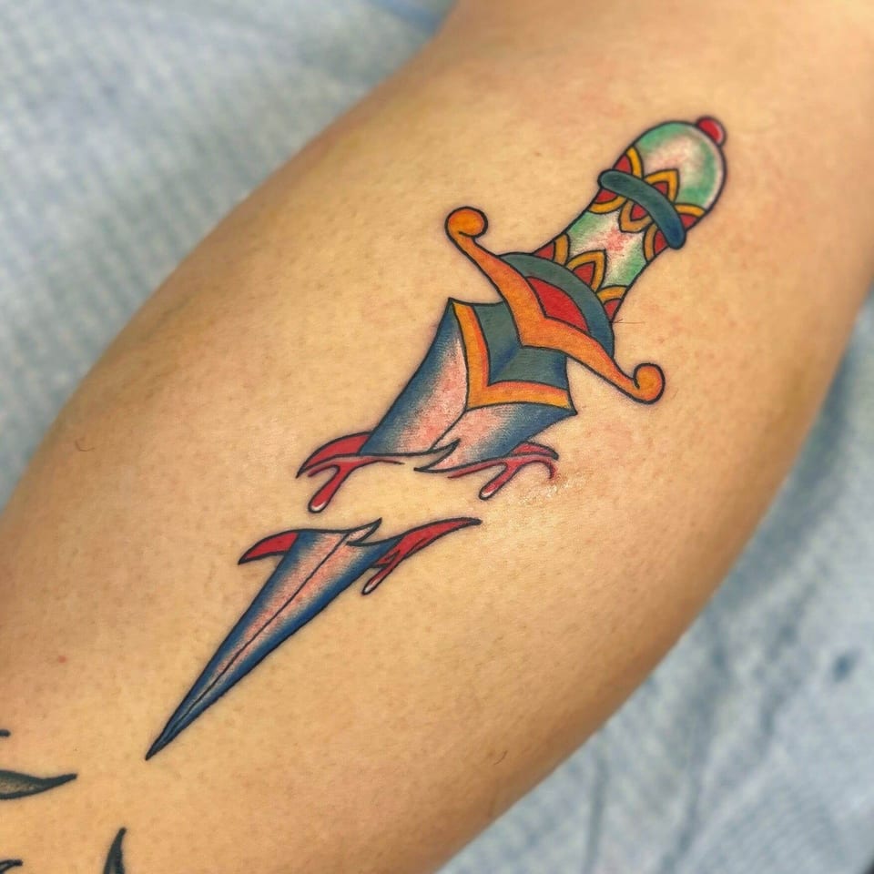 A traditional blue dagger with an orange guard appears to pierce a forearm.