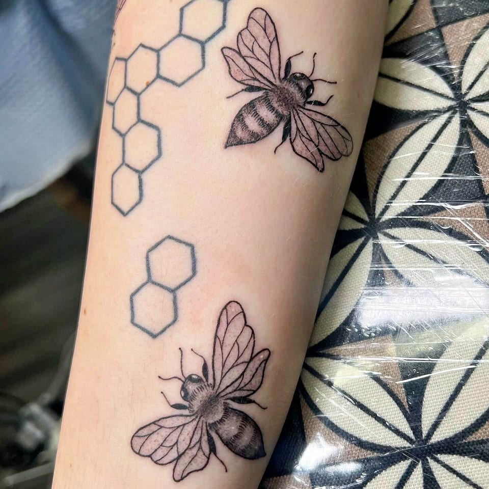 Black and grey bees fly beside honeycomb outlines on a forearm.