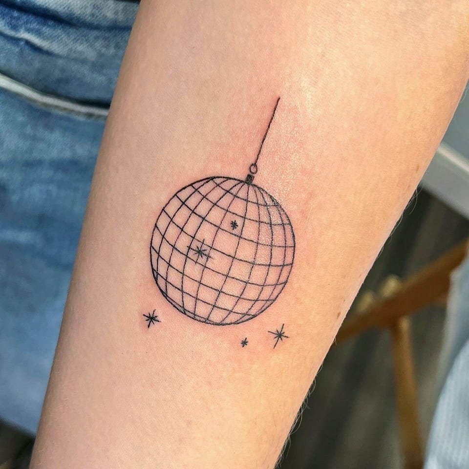 A fine black disco ball hangs above small sparkles on a forearm.