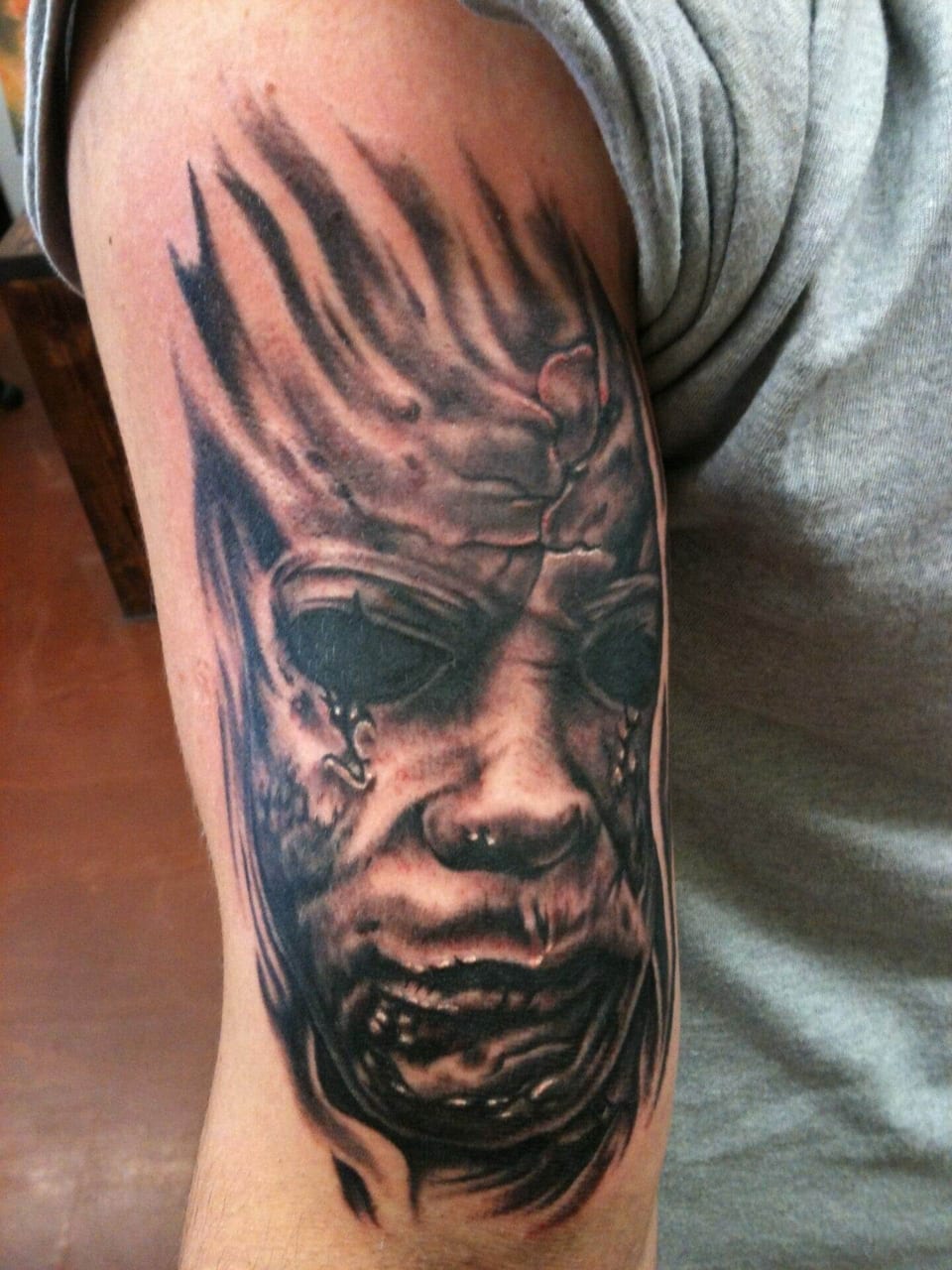 A black and grey distorted face with hollow eyes covers an upper arm.