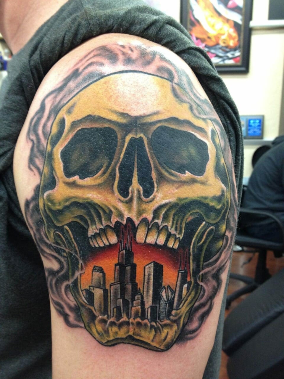 An illustrative colorful skull contains a city skyline within its open jaw tattooed on an upper arm.