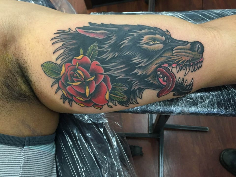 A traditional black wolf with a red rose covers the inner upper arm.