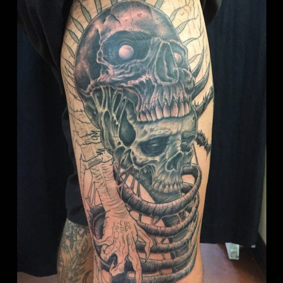 Black and grey skulls sit above skeletal ribs tattooed along an arm.