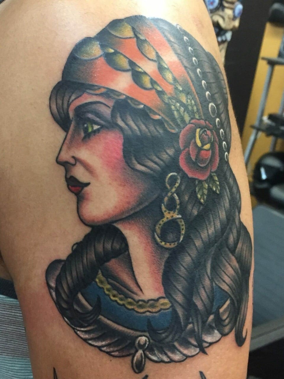 A traditional woman's profile with a patterned headscarf and red rose covers an upper arm.