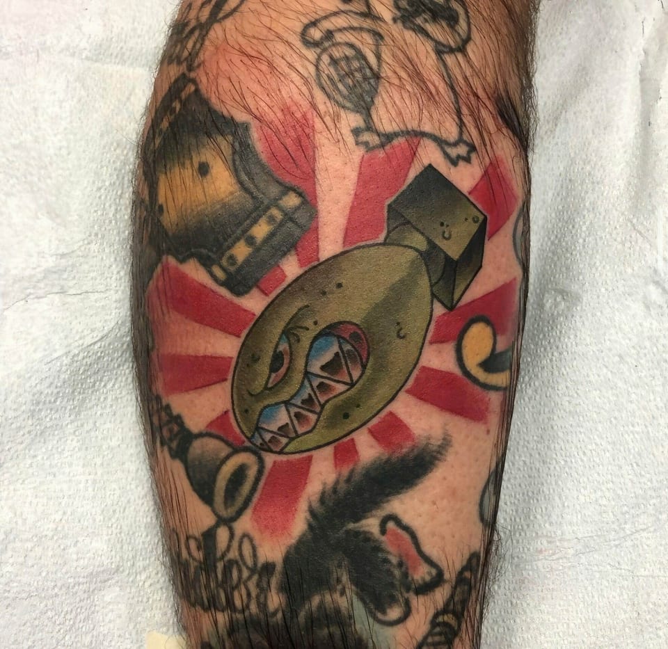 A colorful cartoon bomb sits against red rays in a traditional calf tattoo.
