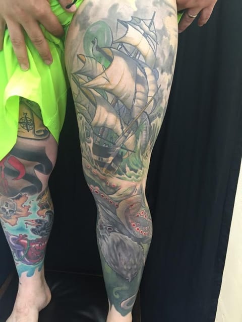 A color illustrative sailing ship and octopus tattoo extends from the thigh to the ankle.