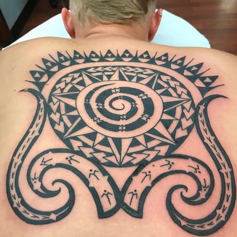 Large Polynesian spiral emblem across a man's upper back, tattooed by Seth Reynolds