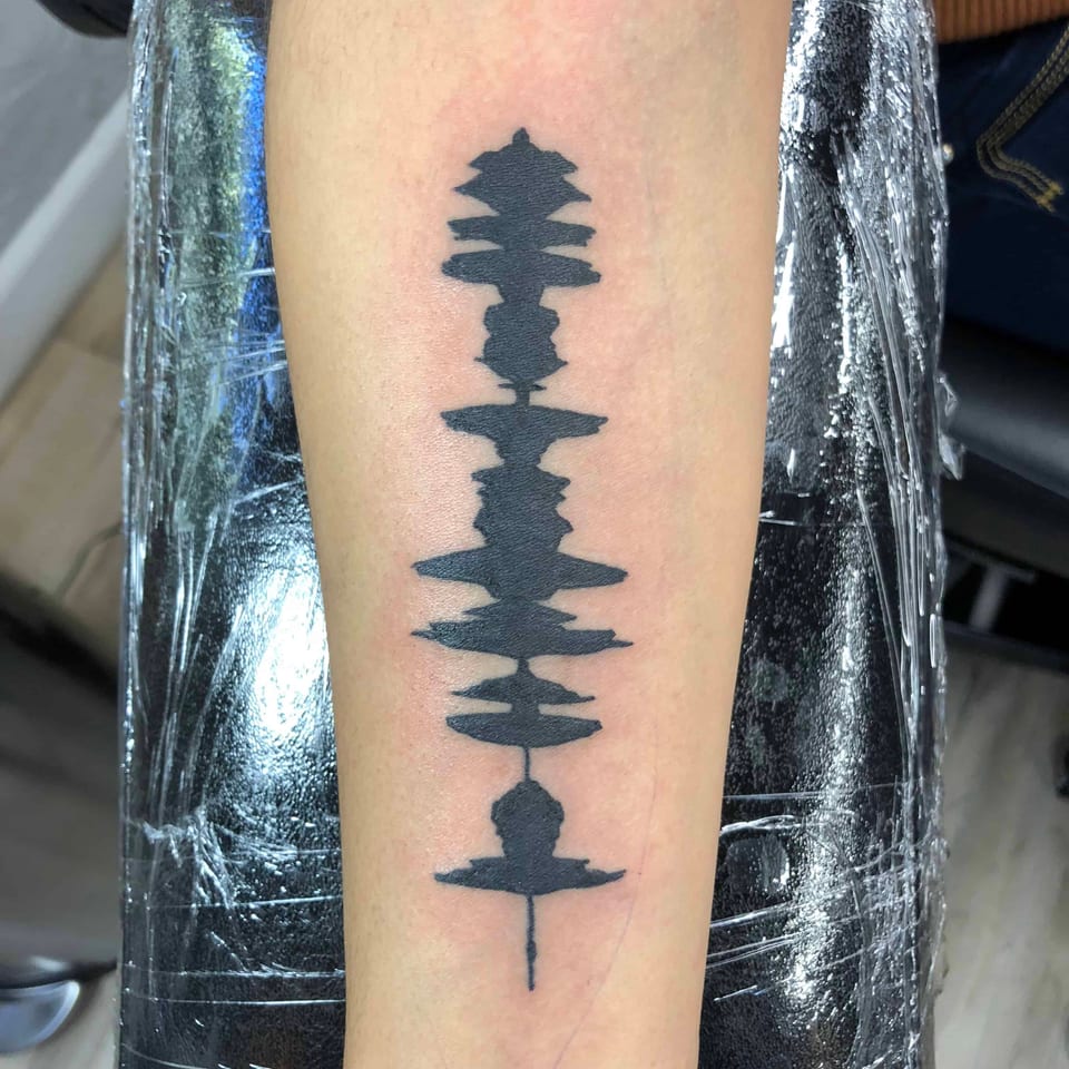 Black soundwave pattern down a forearm, tattooed by Seth Reynolds