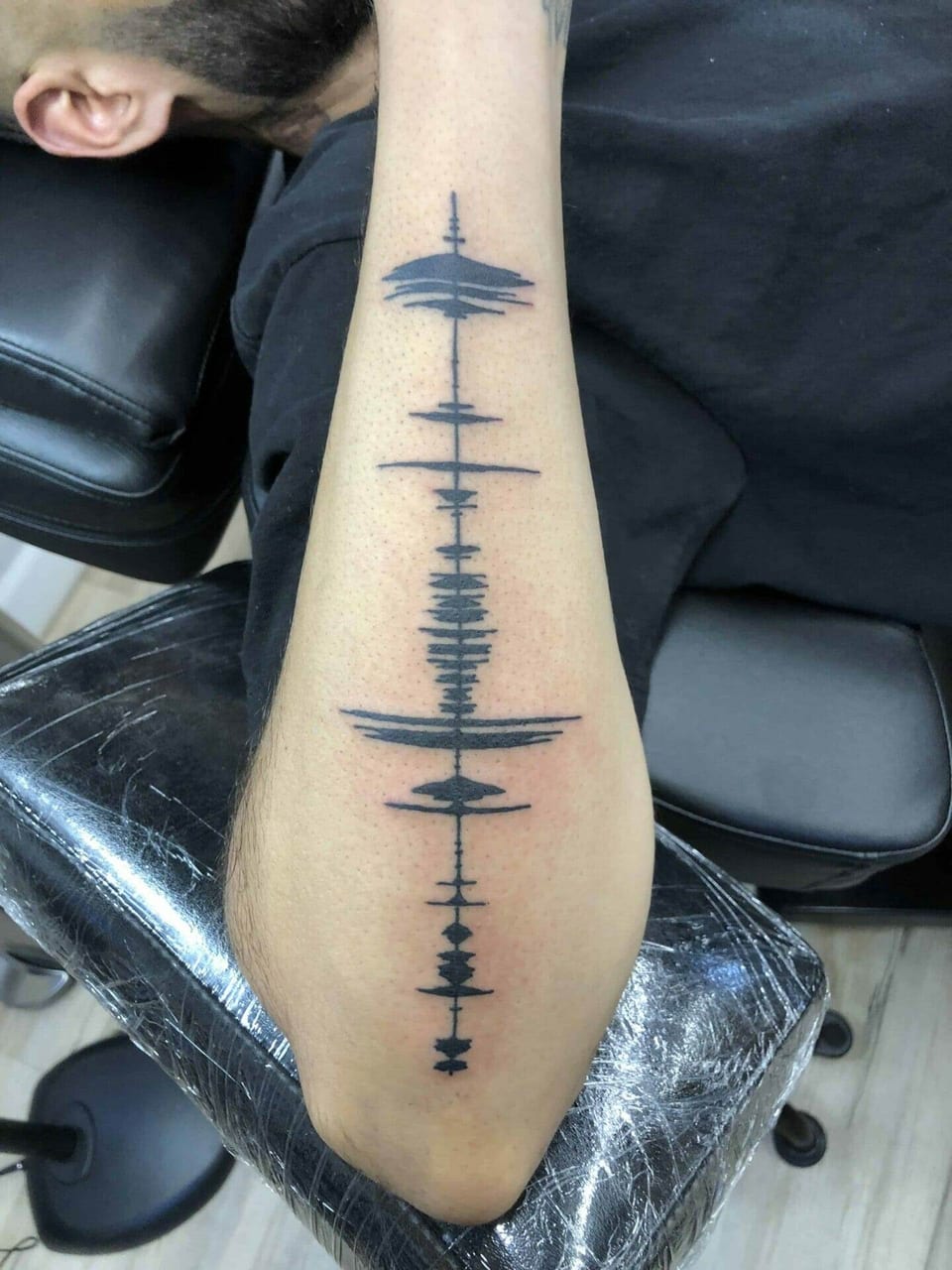 Black soundwave line pattern down a forearm, tattooed by Seth Reynolds