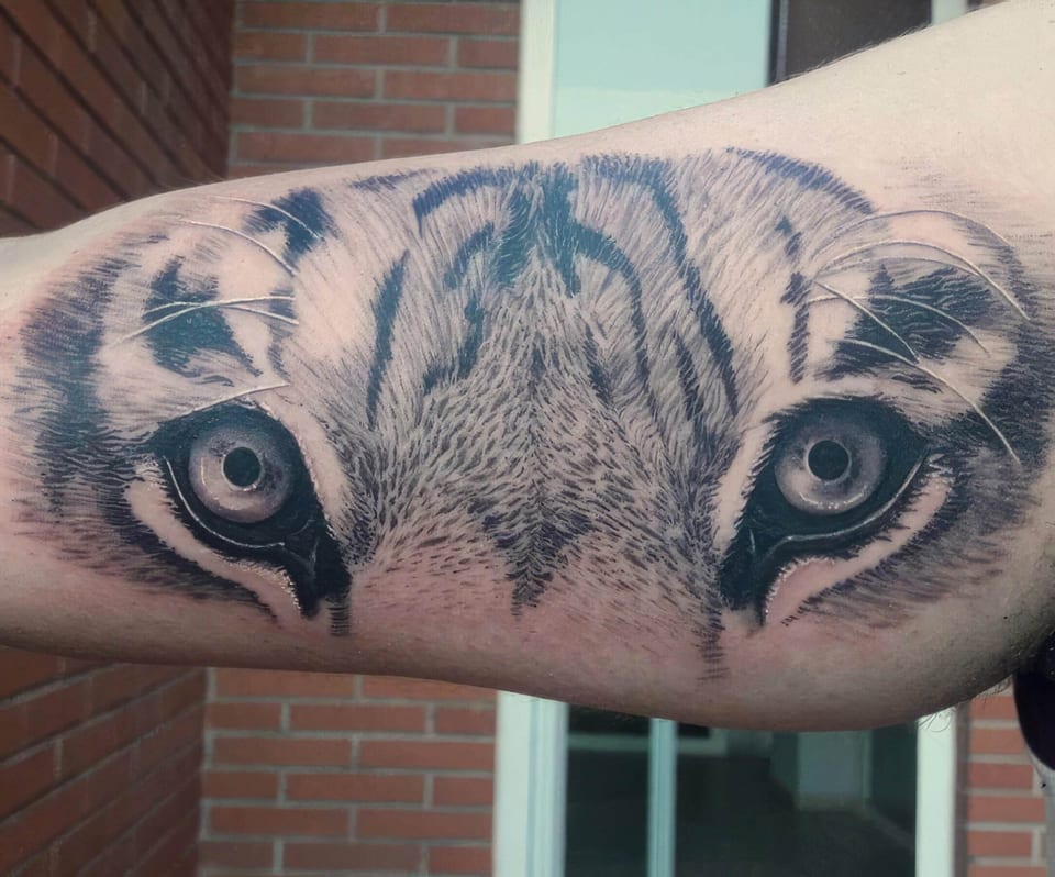 Realistic shaded tiger eyes stare outward from an inner upper arm.