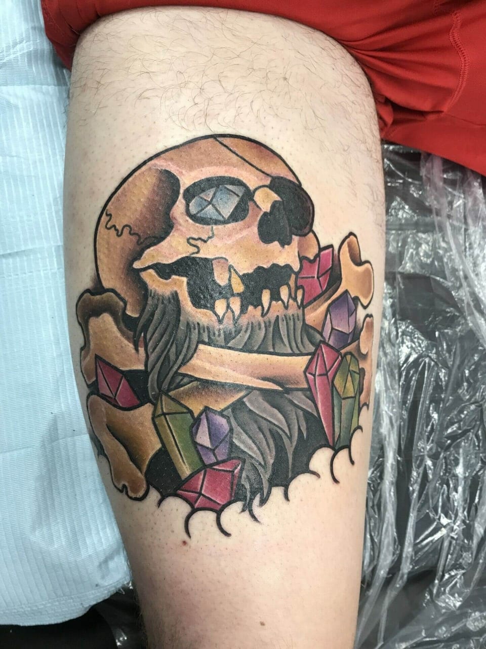 A traditional bearded pirate skull with an eye patch, crossed bones and colorful crystals covers the thigh.