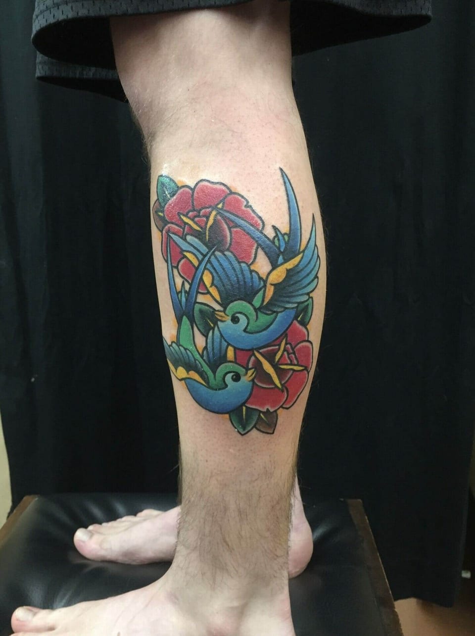 Traditional blue and green swallows fly among red roses on the calf.