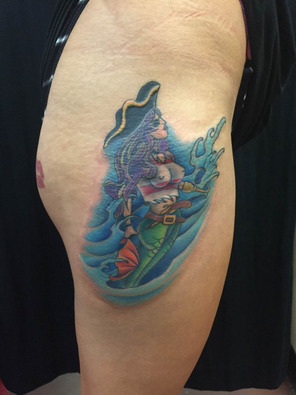 A neo-traditional purple-haired pirate mermaid with a green tail appears against blue waves on the upper arm.