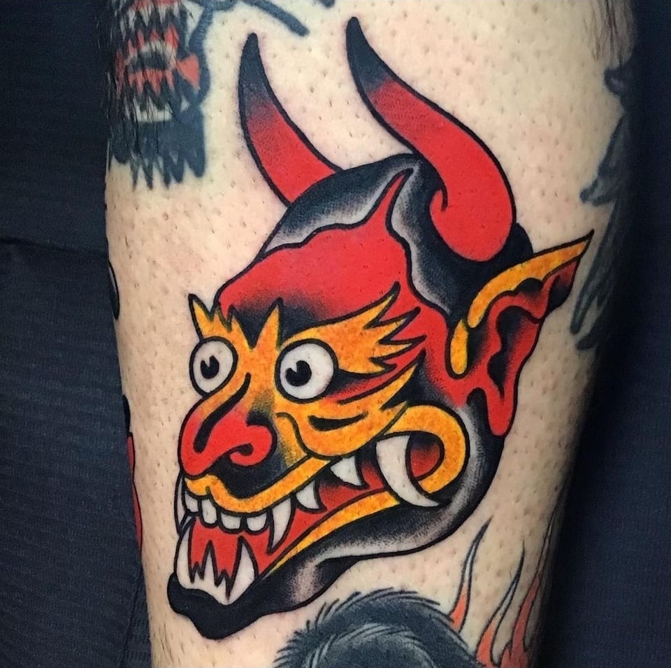 A red and yellow horned devil tattoo bares white fangs.